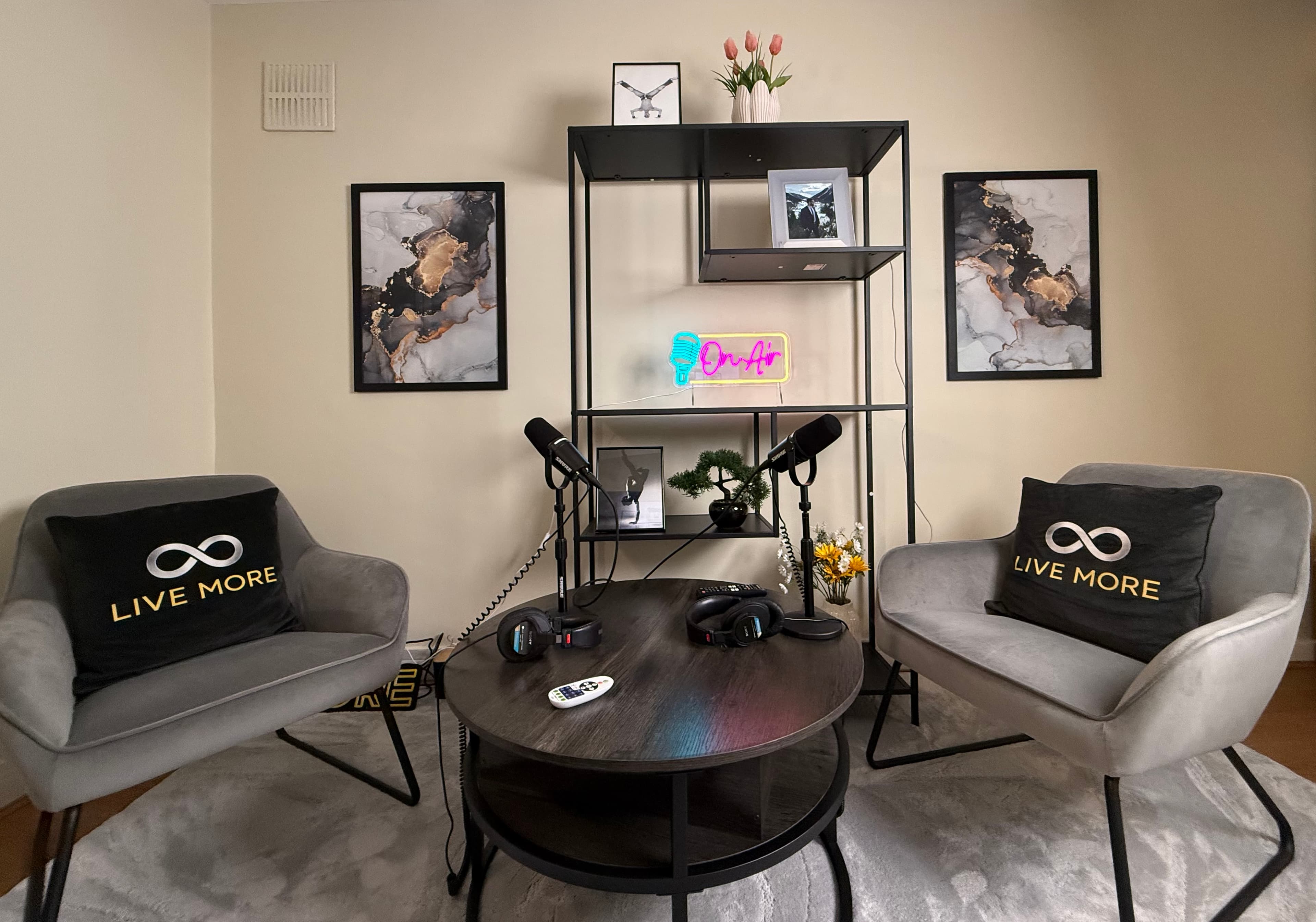 Podcast studio featuring two grey armchairs, microphones, and a neon 'On Air' sign.