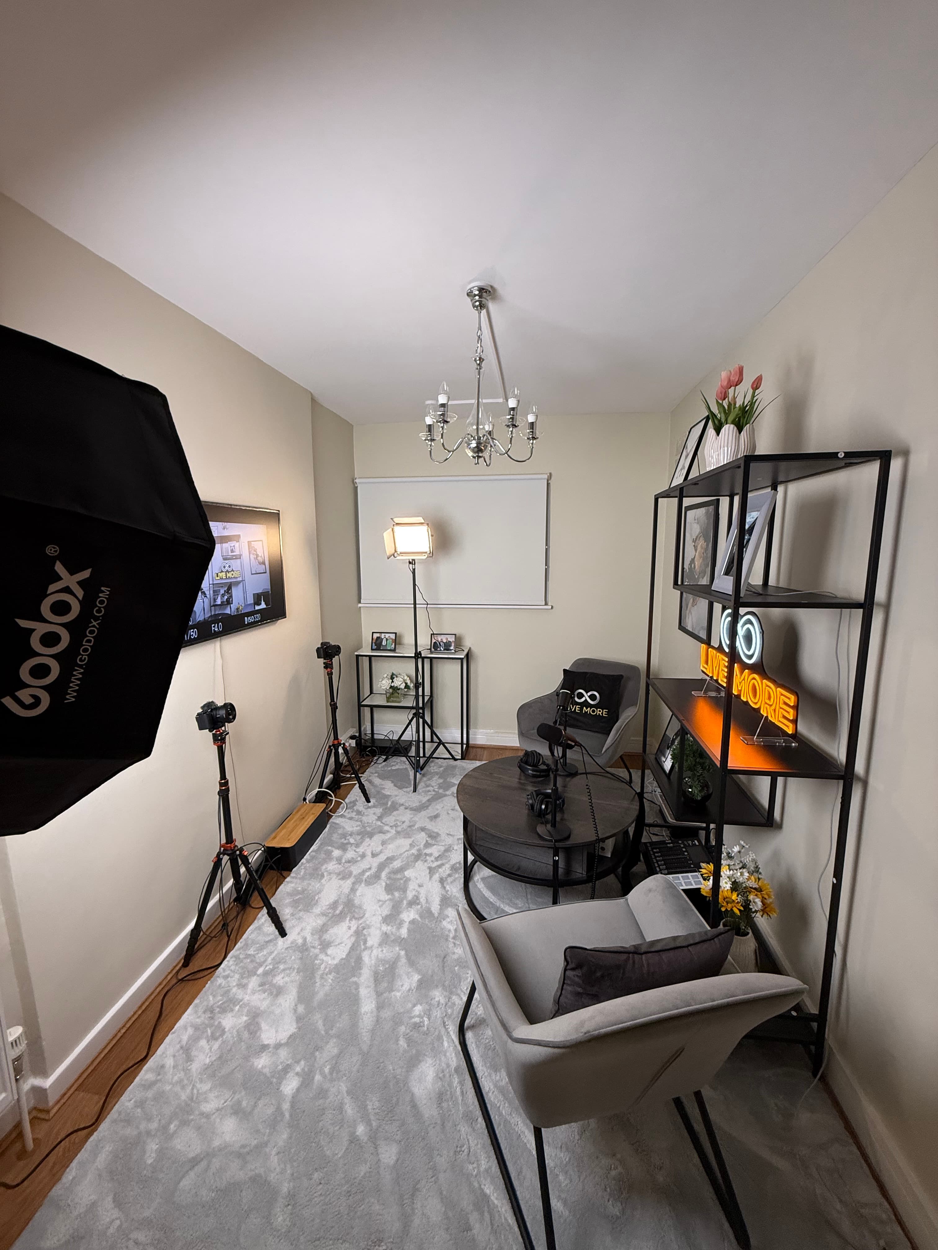 High-angle view of a podcast studio with grey armchairs, microphones, cameras, and a neon sign.