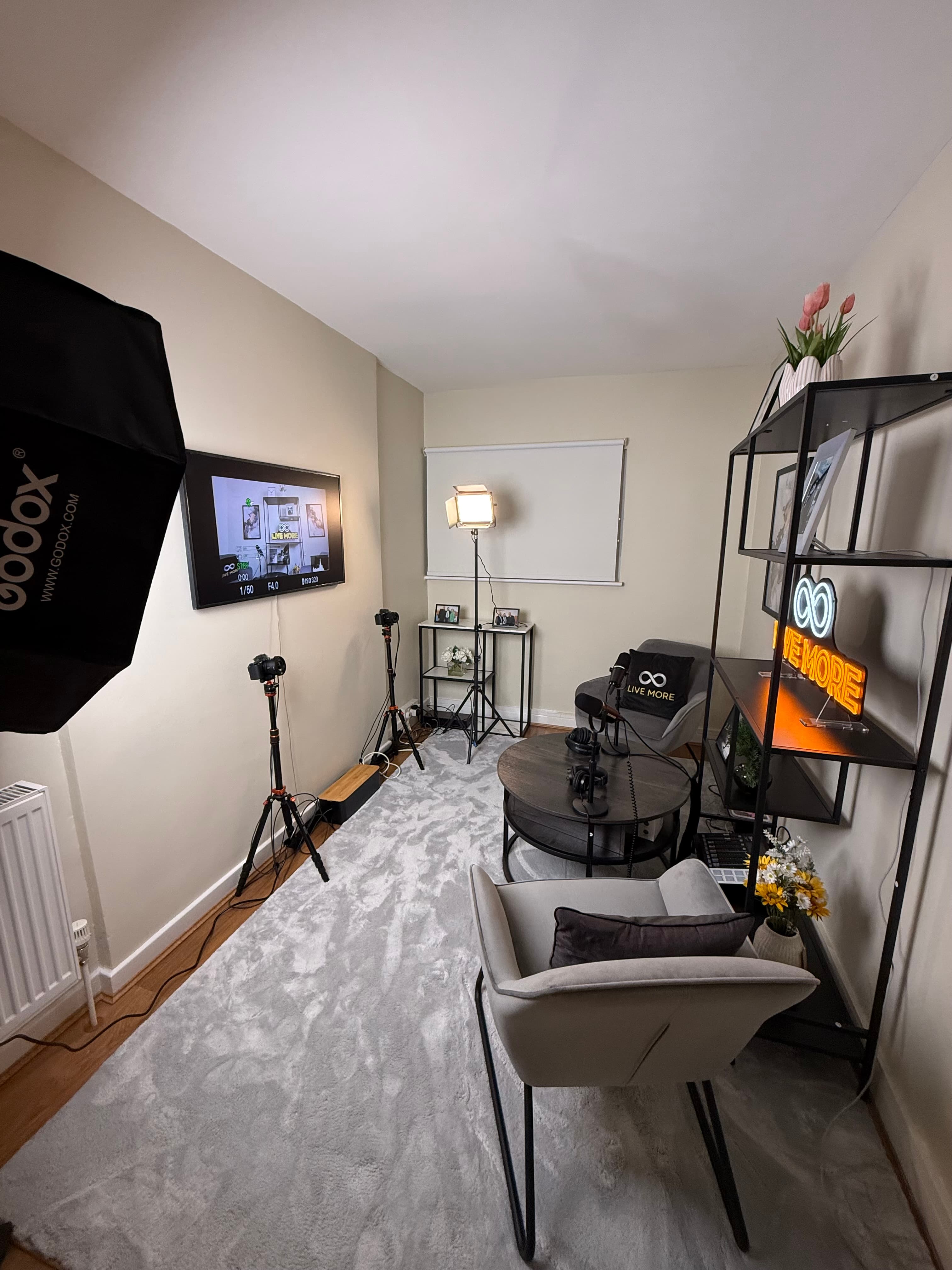 Professional home recording studio with grey armchairs, cameras, microphones, and bright studio lighting equipment.