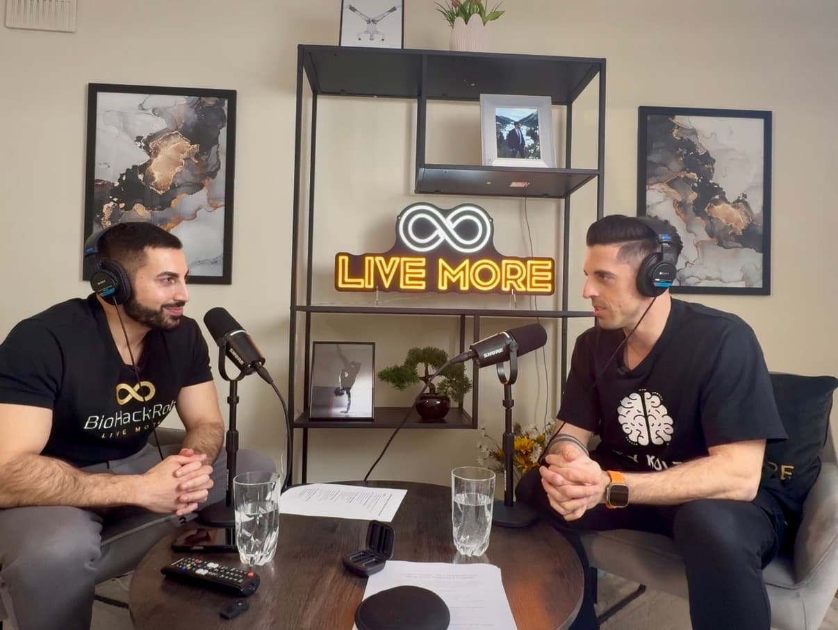 Two men recording a podcast at a table with microphones and a glowing neon sign.