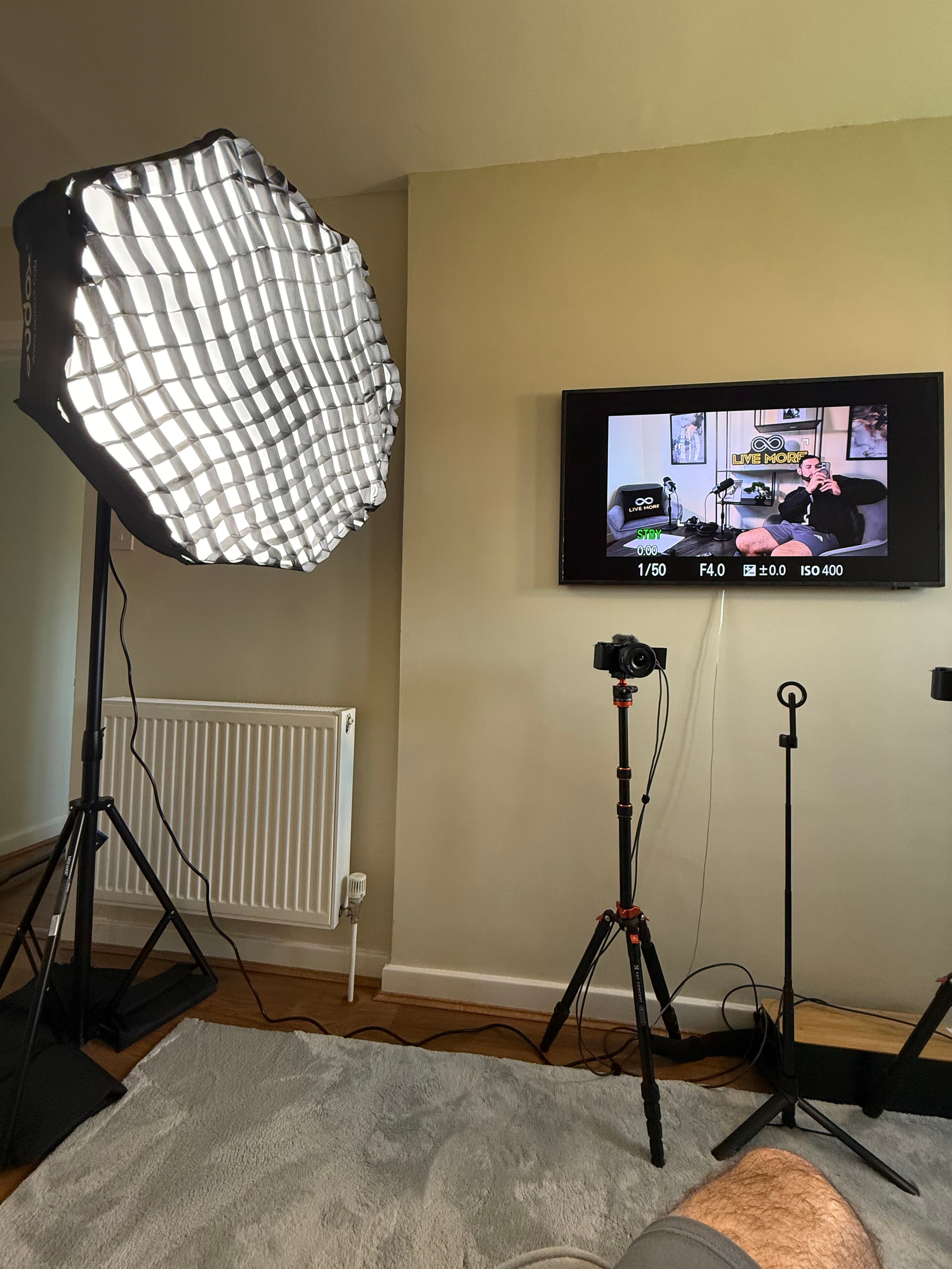 Professional video studio setup with softbox light, camera on tripod, and wall-mounted monitor.