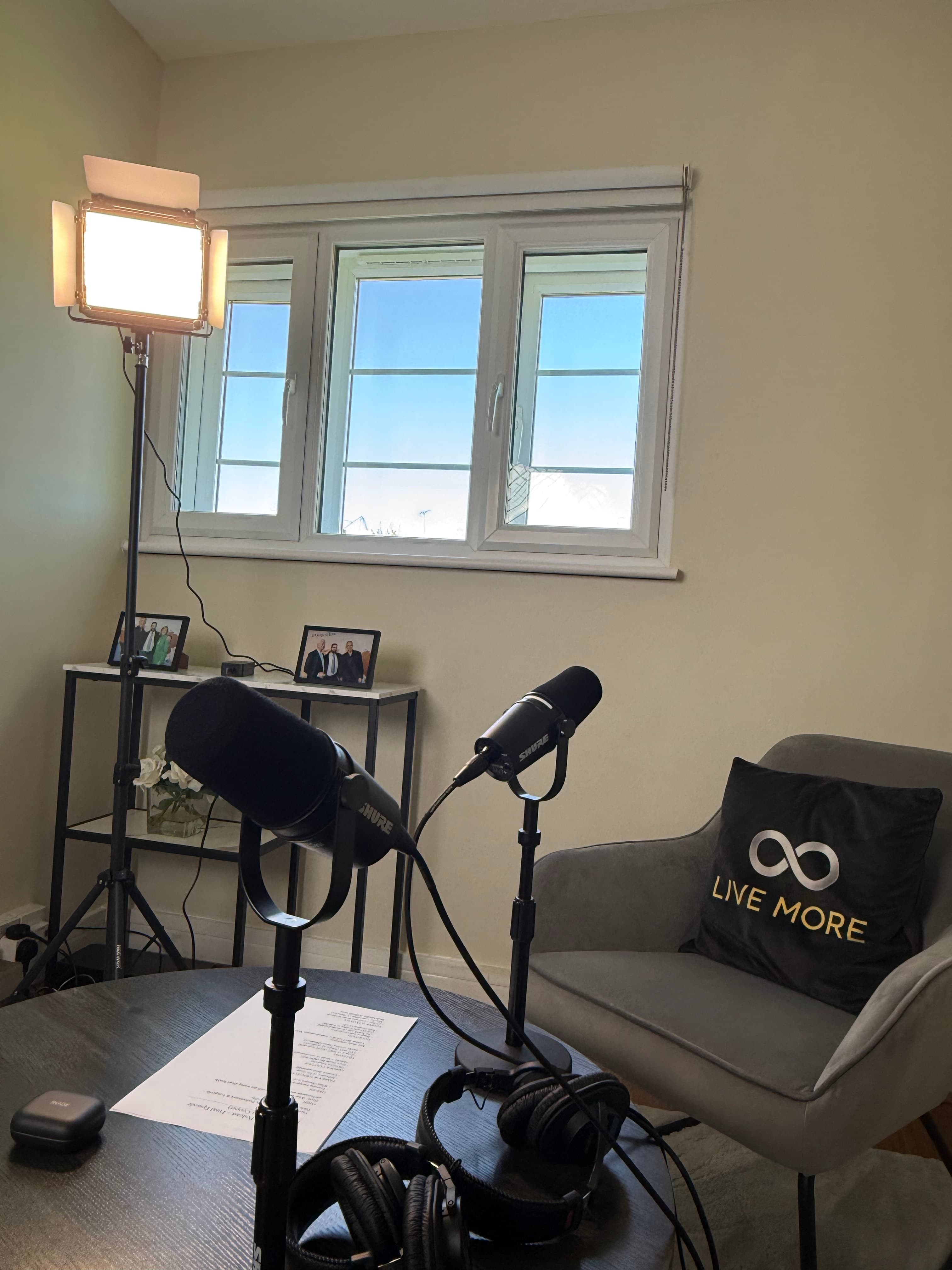 Podcast recording setup featuring two microphones, headphones, a studio light, and a grey armchair.