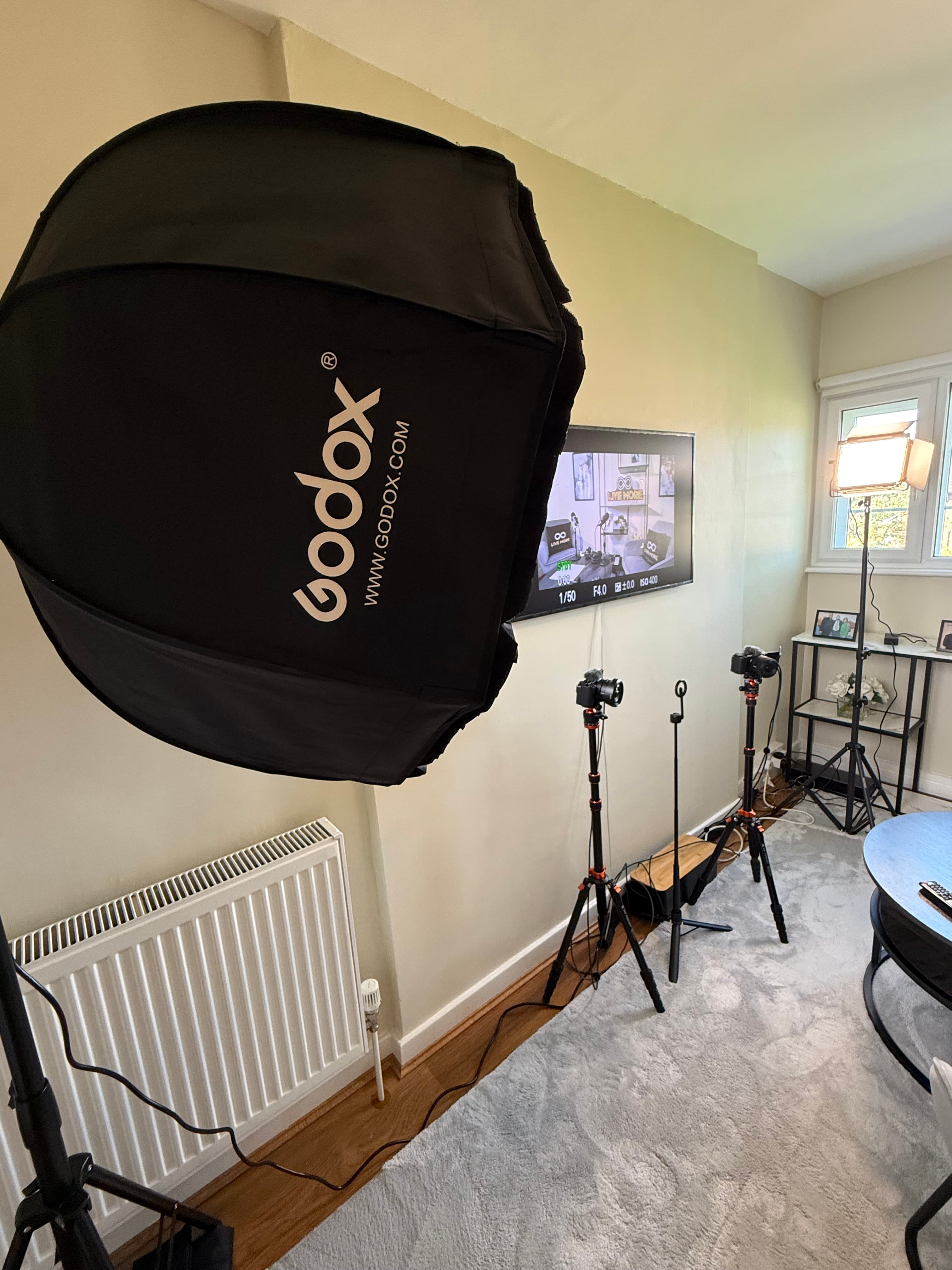 Professional video production setup featuring a Godox softbox, cameras on tripods, and a monitor screen.