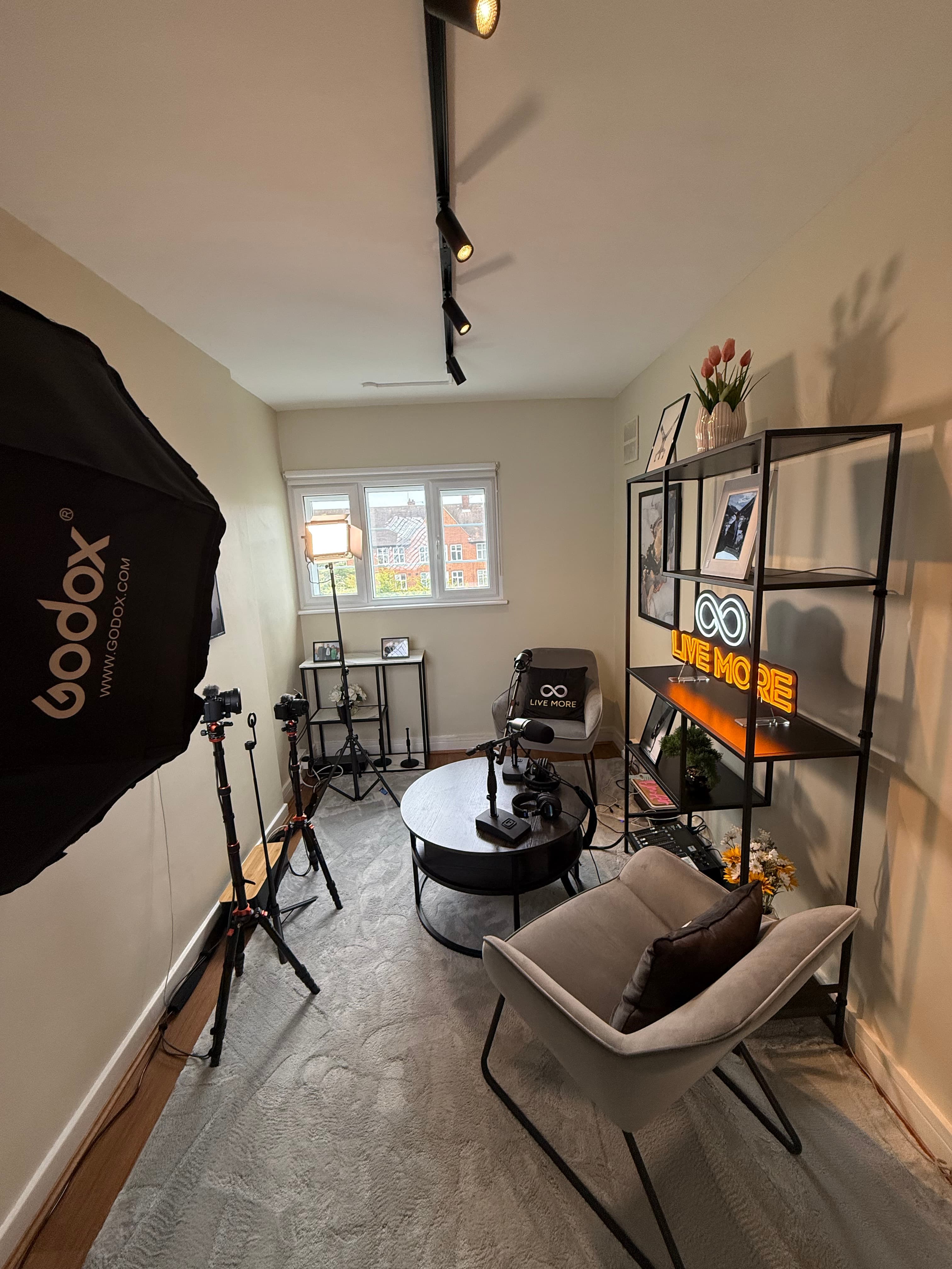 Professional podcast studio with cameras, lighting, armchair, and a glowing "LIVE MORE" neon sign.