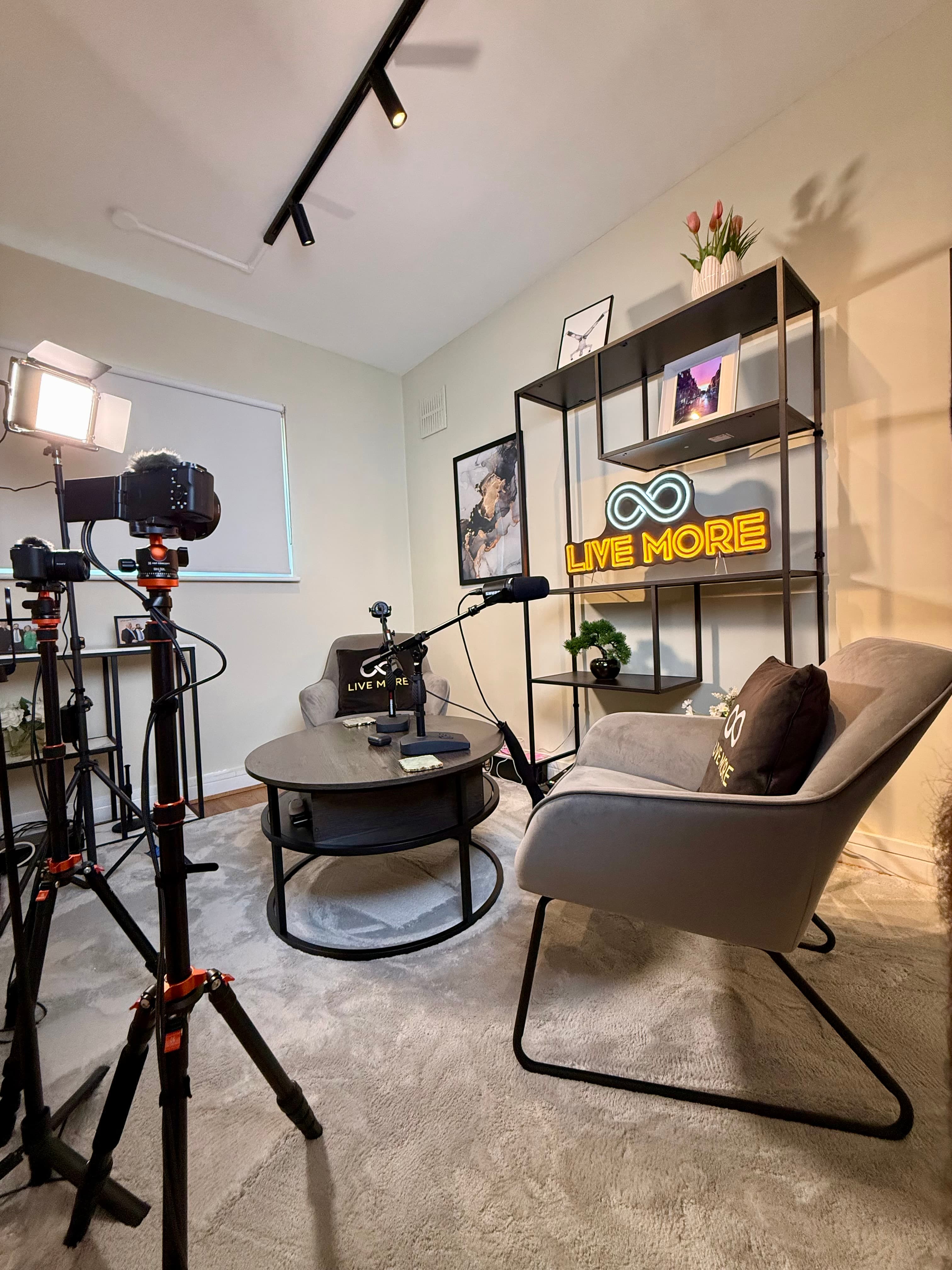 Professional video studio with cameras, microphones, and a neon sign reading "LIVE MORE".